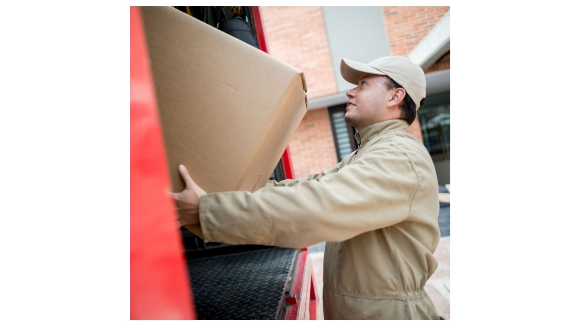 Professional mover in uniform carefully loading a large cardboard box into a moving truck