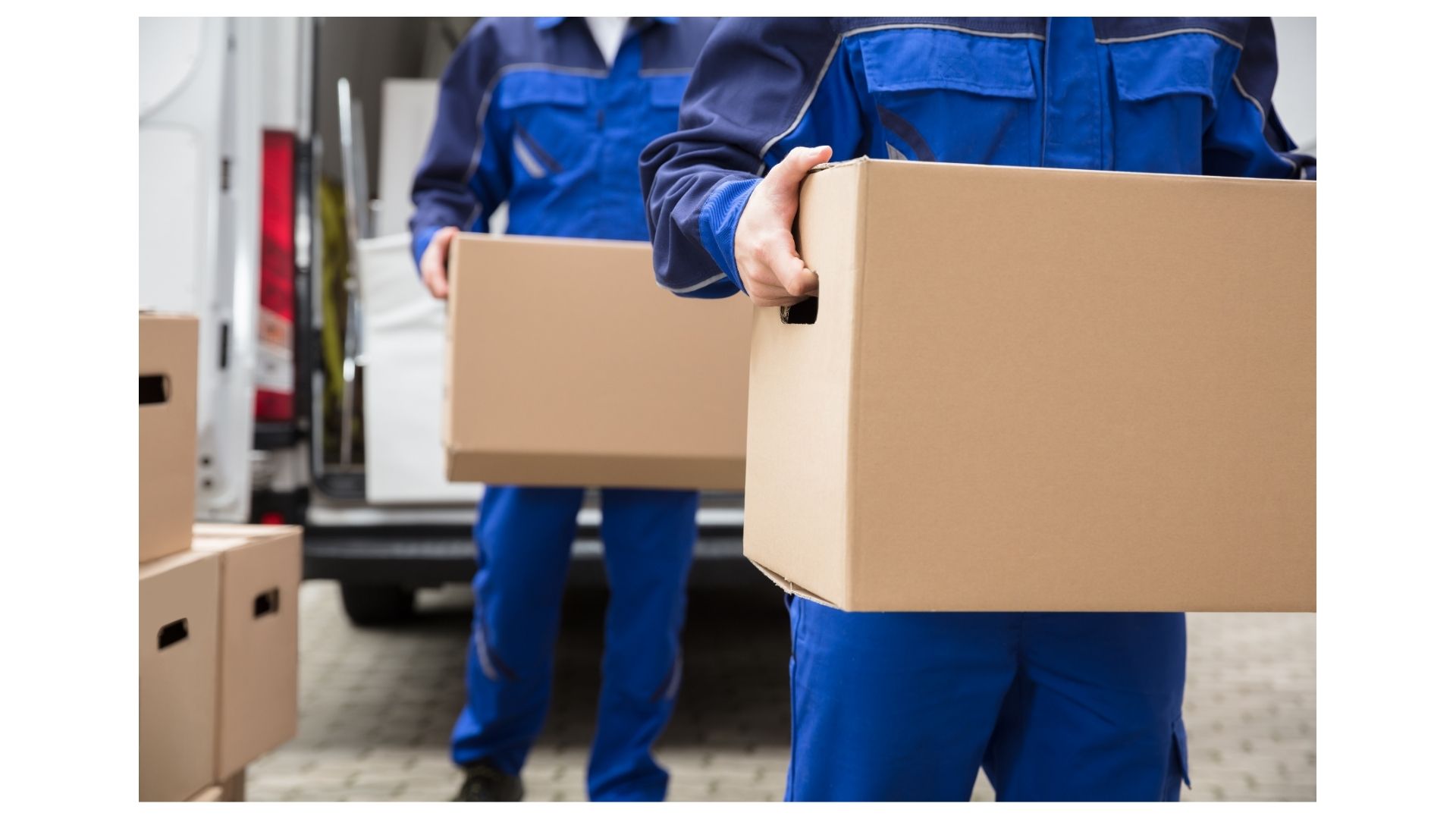 Two movers in blue uniforms carrying cardboard boxes from a white moving van