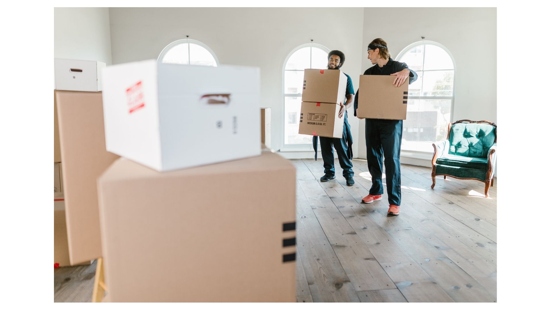 Two Half Price Movers crew members carrying labeled cardboard boxes through a sunlit Texas home
