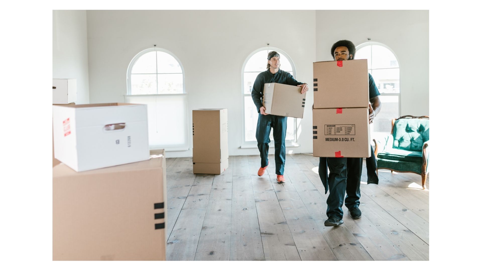 Two movers in a sunlit room carrying labeled cardboard moving boxes for a last-minute evacuation