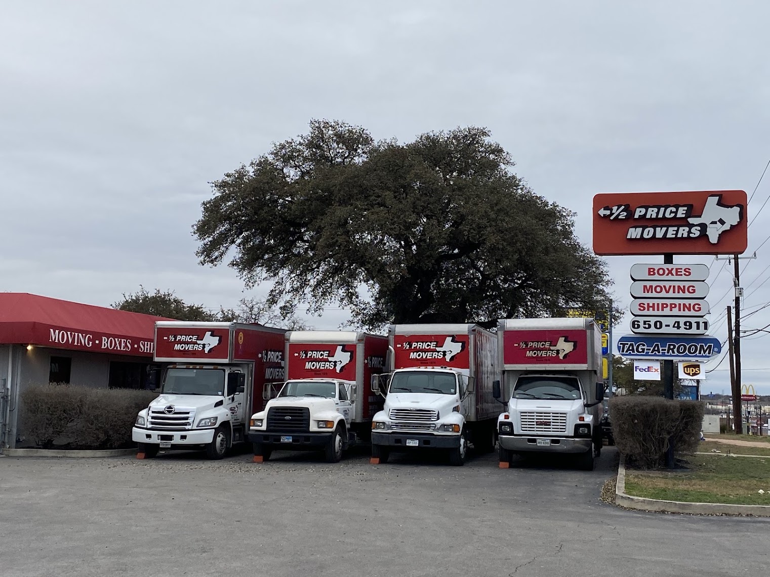 Half Price Movers fleet of branded box trucks parked outside their San Antonio office under a large oak tree