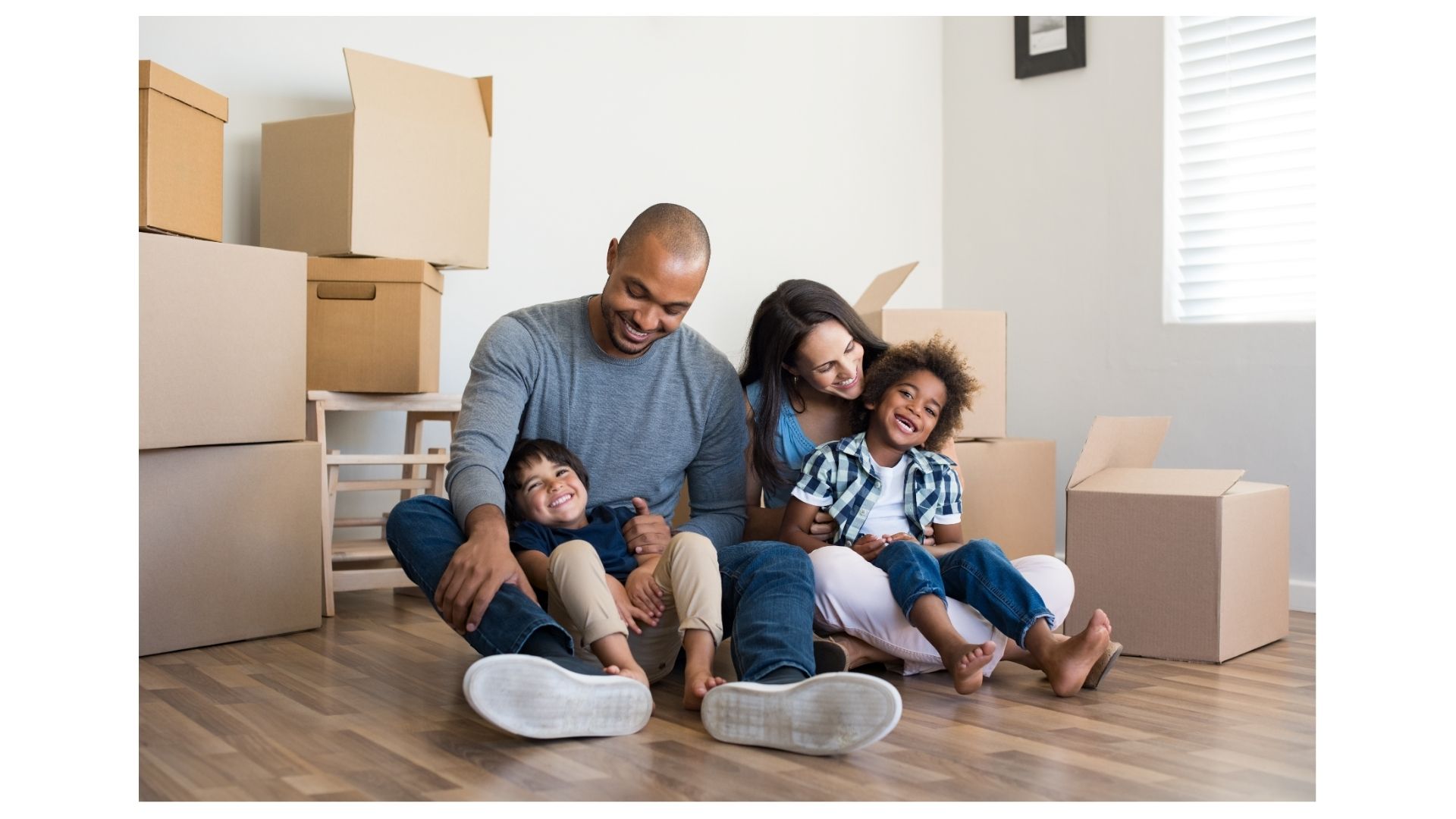 Smiling family with two young children sitting on the floor of their new home surrounded by moving boxes