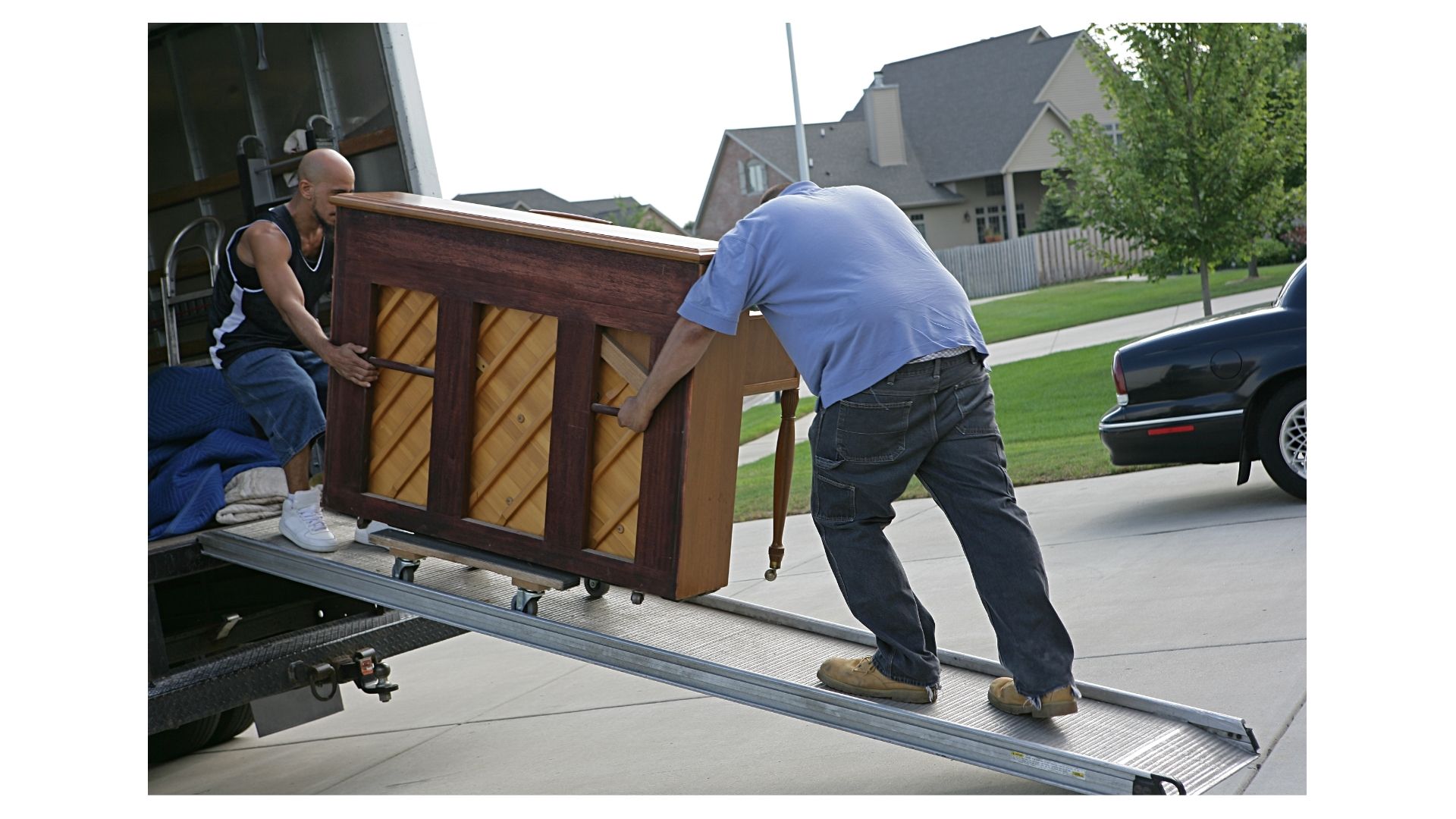 Two professional movers carefully wrapping an upright piano in moving blankets inside a San Antonio home